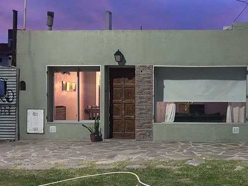 Frente de la casa sobre la avenida Centenario: pared verde, puerta de madera, ventana y ventanal, con vereda de piedra