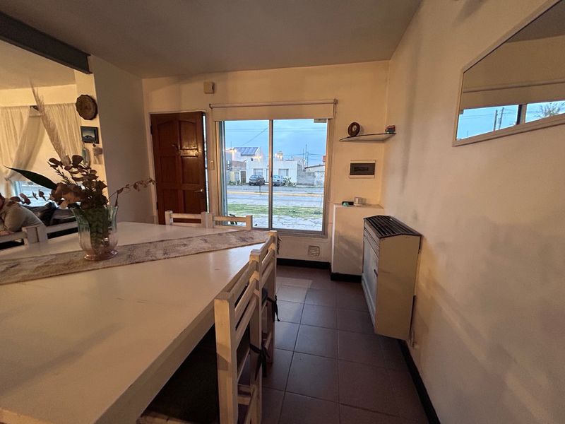 Comedor con mesa y sillas blancas, cocina integrada al fondo