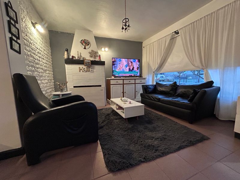 Living con sillones oscuros, hogar blanco y ventanal con cortinas